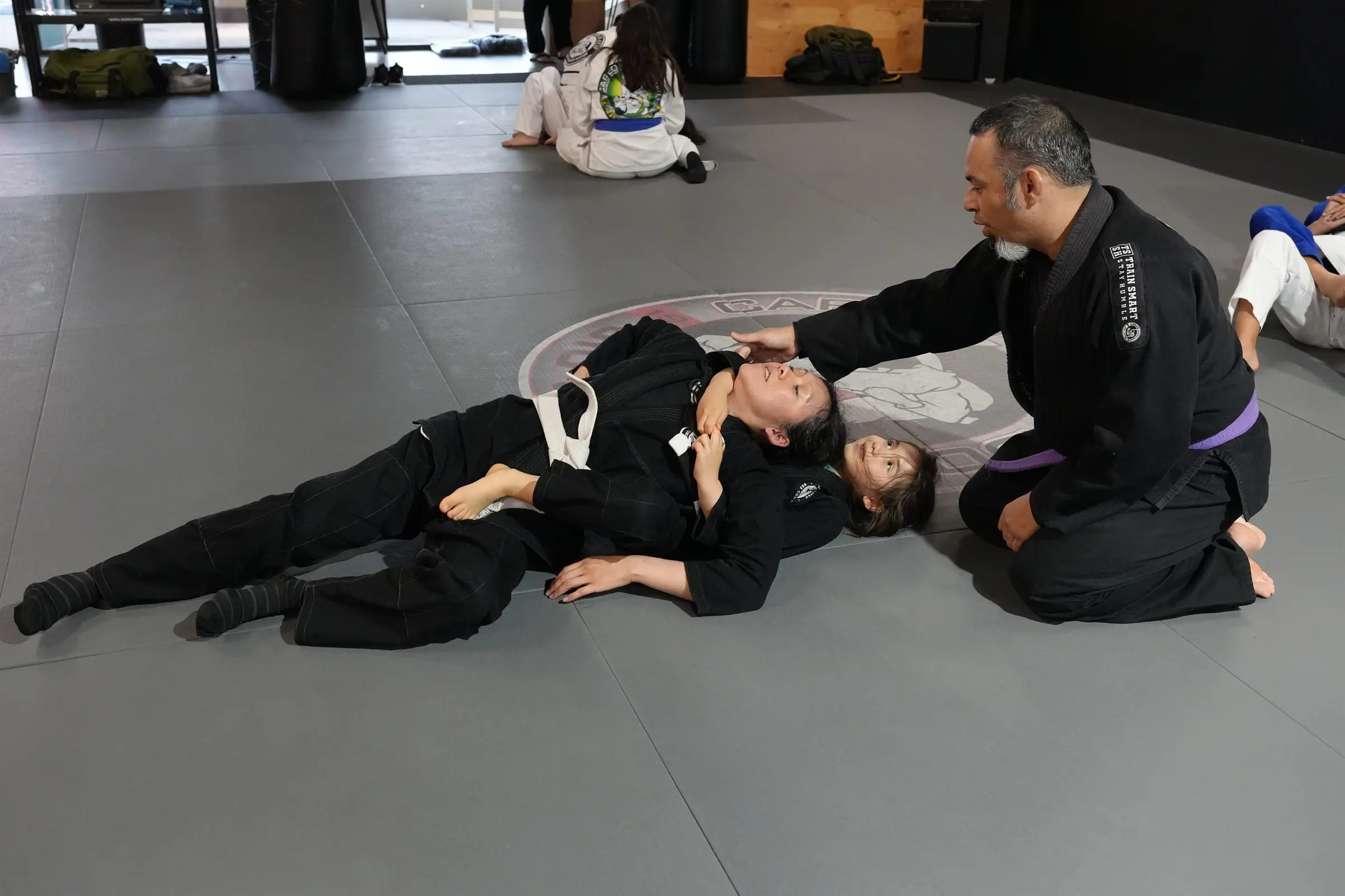 A coach guiding two women through a Brazilian Jiu-Jitsu technique at 805 Combat Sports in Simi Valley